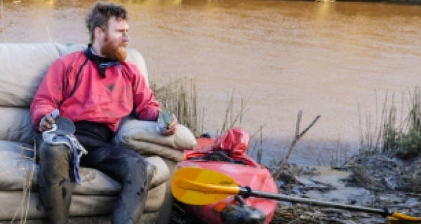 Beau Miles sitting on couch with river in back and kayak