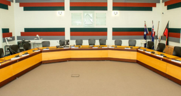 Council Chambers - brown wooden desks set up in a u-shape with chairs around the back side