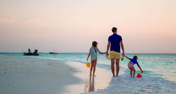 Father walking along beach holding hands with his children