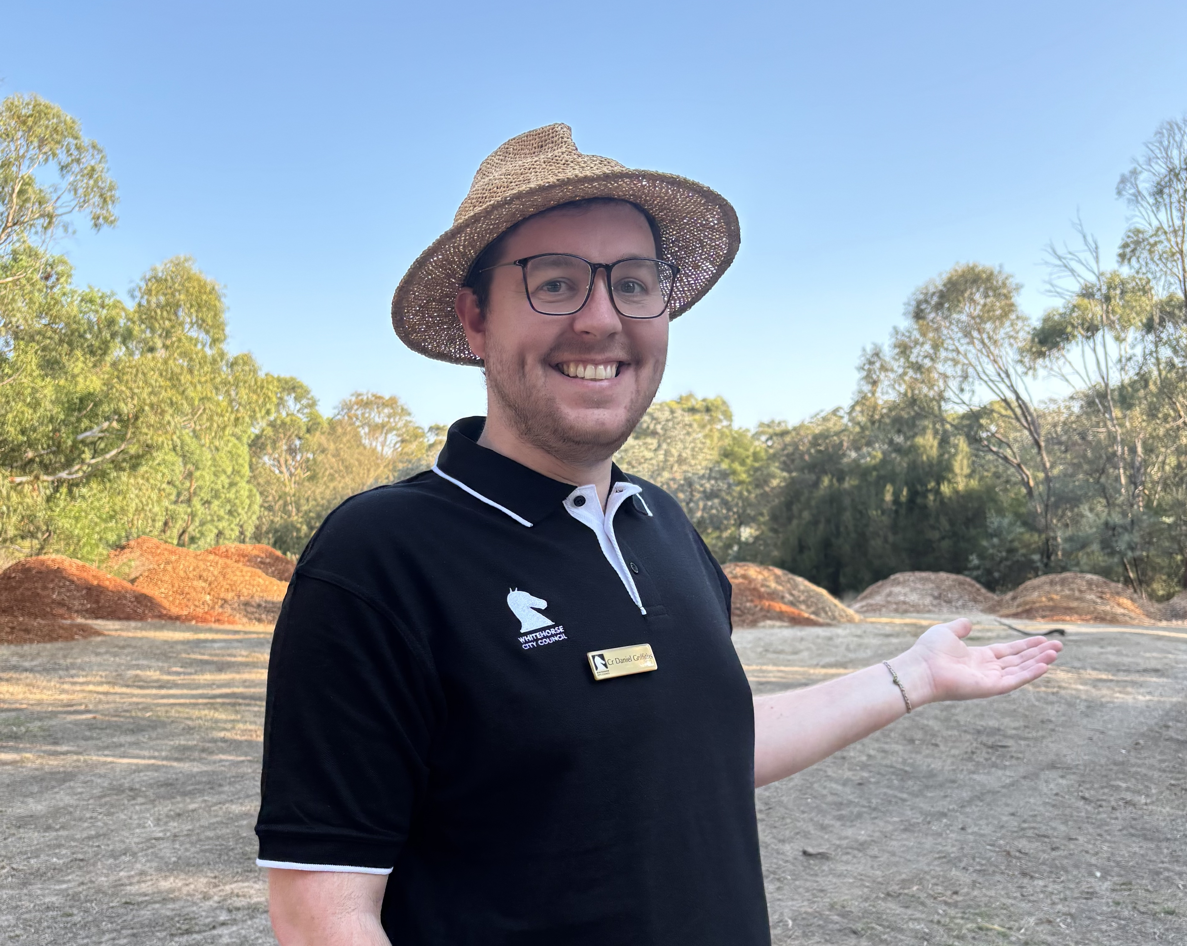 Cr Griffiths standing in an open space pointing at large piles of mulch behind him