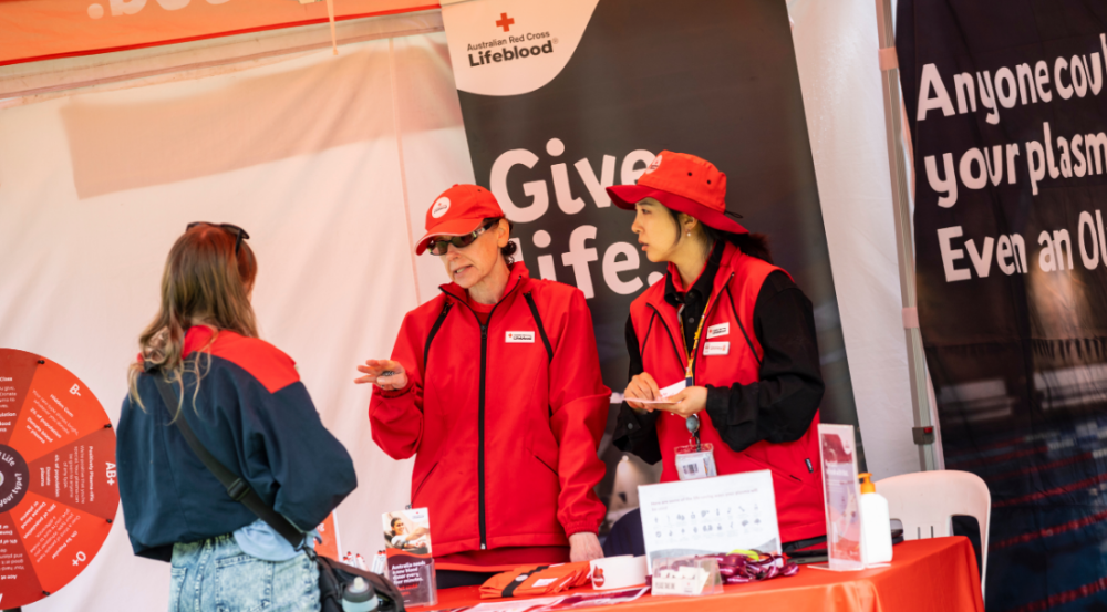 two women in red talking with a person who's stopped at their stall