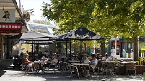 looking down Britannia Mall with shops on the left and people sitting on tables in the mall