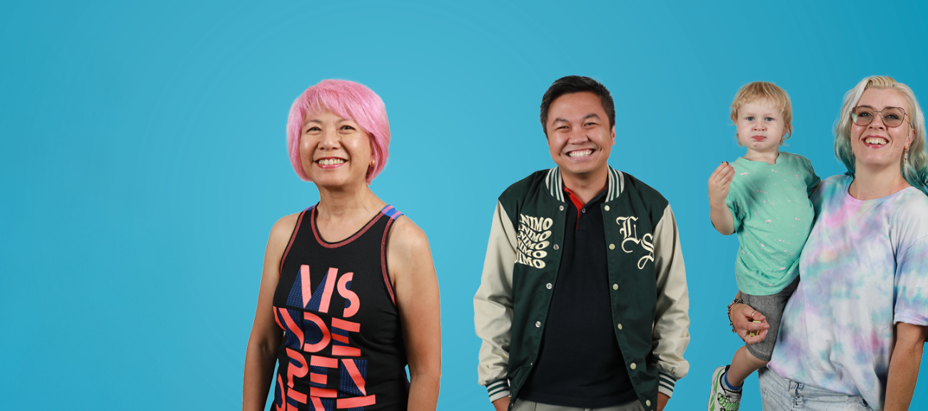 3 people and a baby standing in front of a blue background smiling. 