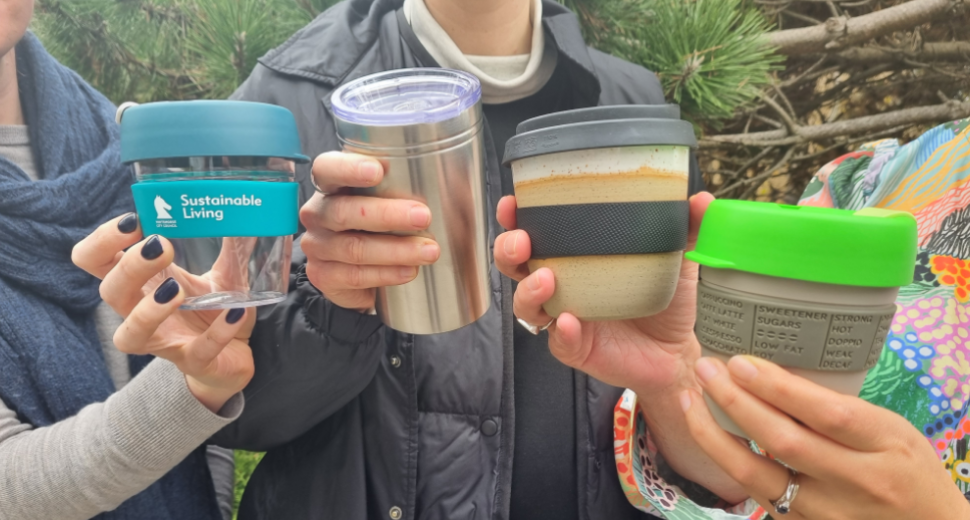 four hands holding a reusable coffee mug each holding them up to the camera in a cheers motion