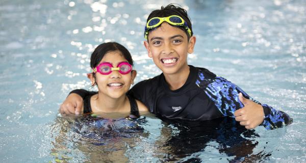 Kids in the pool smiling at the camera 