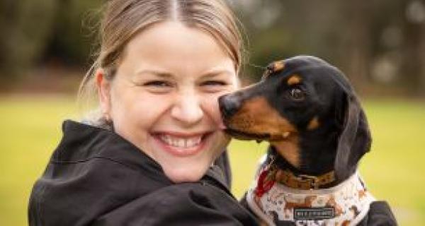 Girl holding a sausage dog beside her face on the right. 