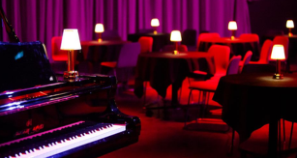 dark room with purple curtains on the walls with small tables with lamps and a piano in the foreground