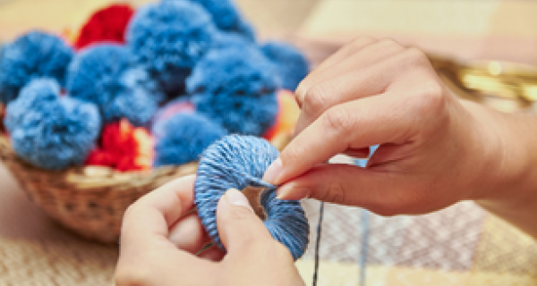two hands threading blue yarn around a carboard ring to make pom poms