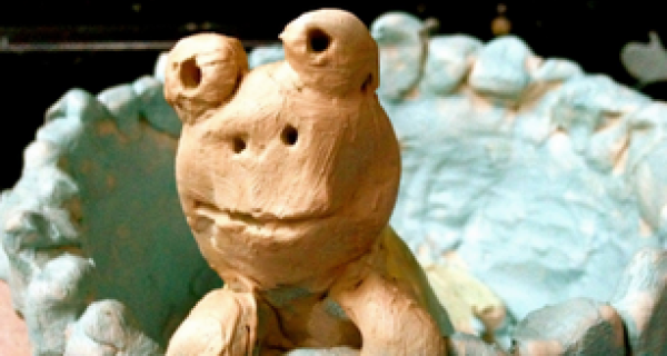 A hand carved clay frog resting on the edge of a blue clay bowl
