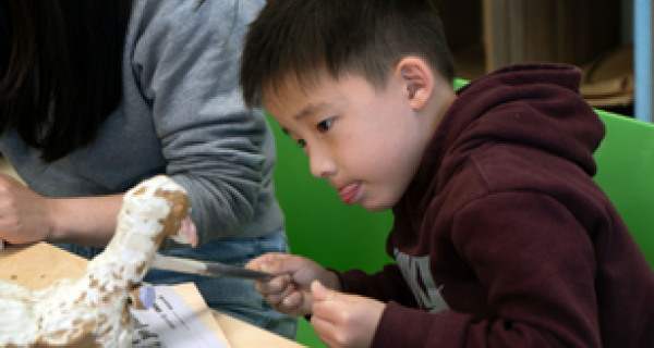 young child carving a clay animal with a metal tool