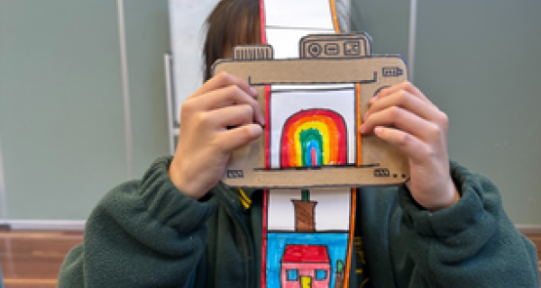 Child holding up a cardboard polaroid camera over their face 