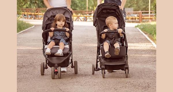 two parents walking side by side with their young children in prams