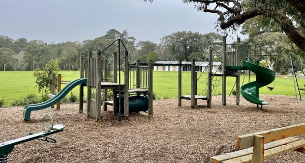 The playground at Kalang Park Play Space including wooden play equipment with 2 slides and a swing set.  