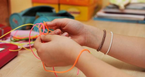 Close up of hands weaving with coloured material 
