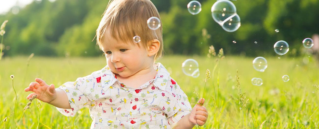 Young child sitting in the grass with bare feet trying to catch bubbles
